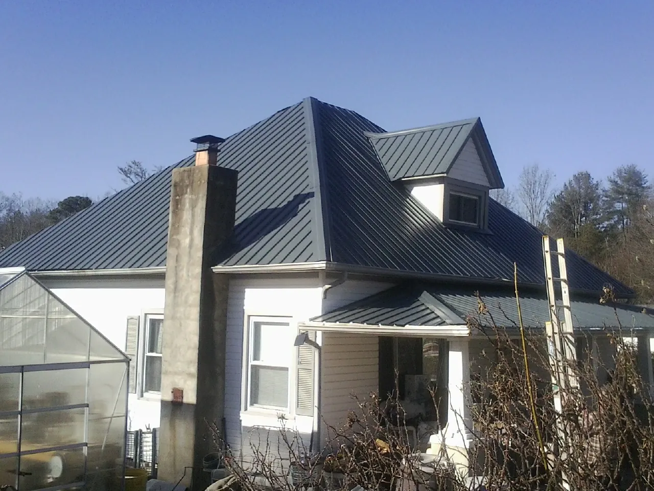 Dark blue standing seam metal roof on a white farmhouse with dormer — Slate & Tile Roof Repair by Roofing Brothers in D Lo