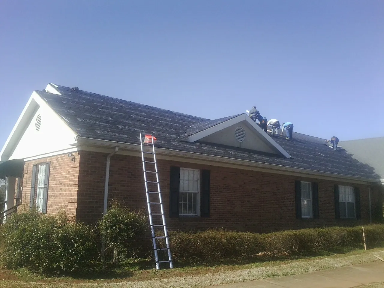 Crew tearing shingles off a brick ranch roof with a ladder set — Metal Roof Repair work by our crew in D Lo