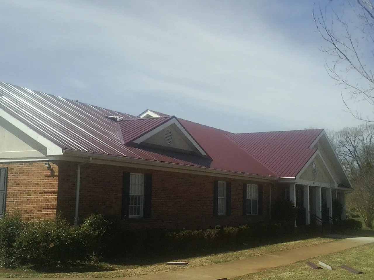Red metal roof with gabled entries on a long brick building, from a Hail Damage Roof Repair job in D Lo