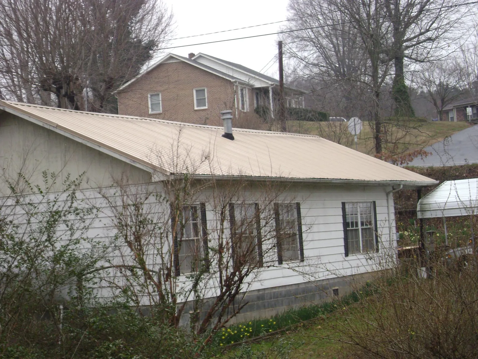 Tan metal roof on a white sided house set into a hillside — Commercial Roofing by Roofing Brothers in D Lo
